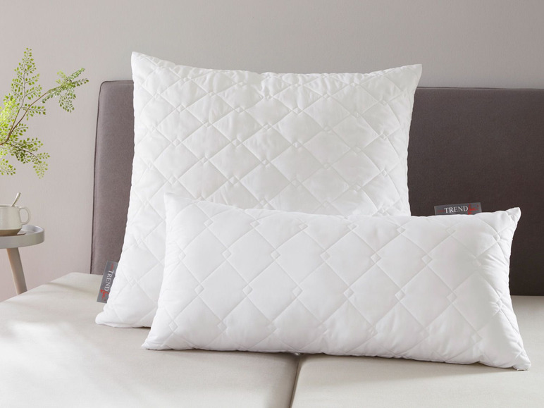 Zwei weiße Trend Kissen mit Rautenmuster auf einem Bett.