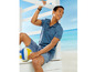 Mann in einem blauen Poloshirt und Shorts mit einem Volleyball am Strand.