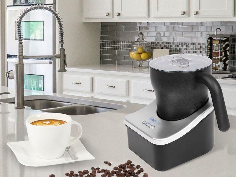 Ein automatischer Milchaufschäumer, eine Tasse Cappuccino und Kaffeebohnen in einer Küche.