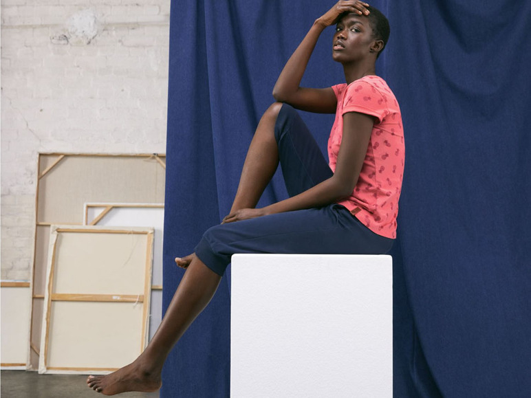 Eine Frau trägt ein rosa T-Shirt mit Ananas-Print und blaue Hosen.