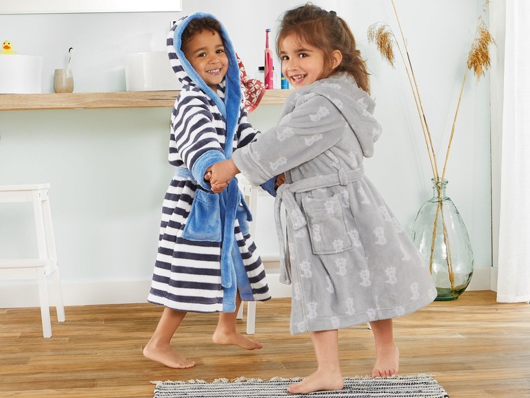 Zwei Kinder tragen Bademäntel, einer mit blauen Streifen und einer mit Tierprint.