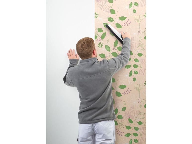 Ein Mann klebt eine Tapete mit Blumenmuster an eine weiße Wand.