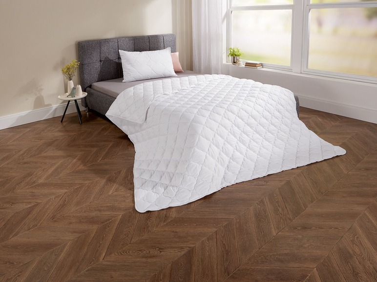 Eine weiße Bettdecke auf einem Bett mit grauem Kopfteil.