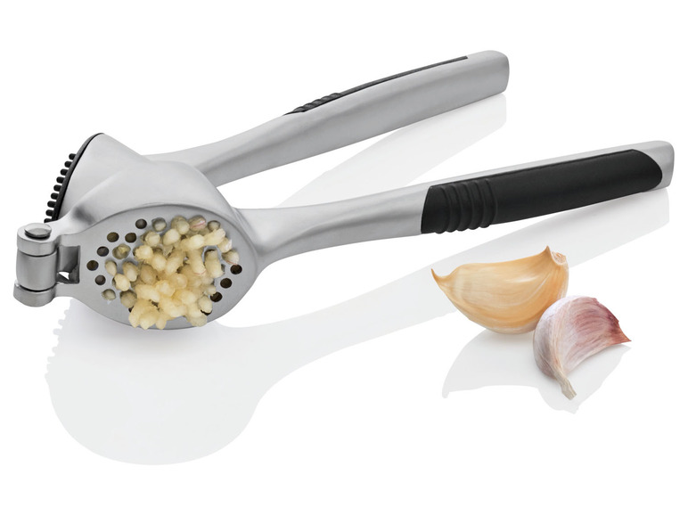 Eine Knoblauchpresse mit gepresstem Knoblauch und zwei Knoblauchzehen.