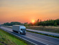 Ein weißer LKW fährt bei Sonnenuntergang auf einer Autobahn.