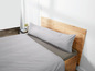 Ein graues Kissen auf einem Bett mit einem Holz-Kopfteil.