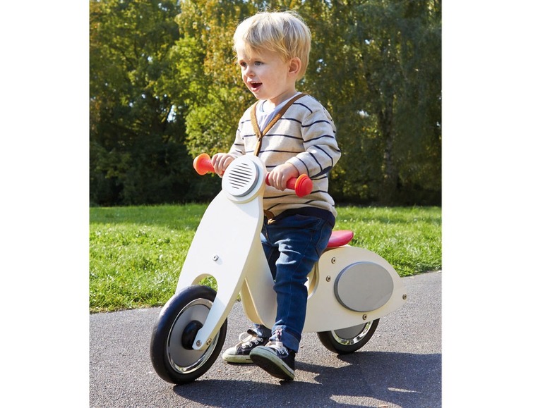 Ein Kind fährt ein hölzernes Laufrad in Form eines Scooters.