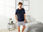 Mann in einem dunkelblauen T-Shirt und grauen Pyjama-Shorts mit Muster