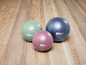 Drei Fitnessbälle in verschiedenen Farben auf einem Holzboden.
