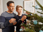 Ein Vater und sein Sohn schmücken einen Weihnachtsbaum mit blauen und goldenen Kugeln.