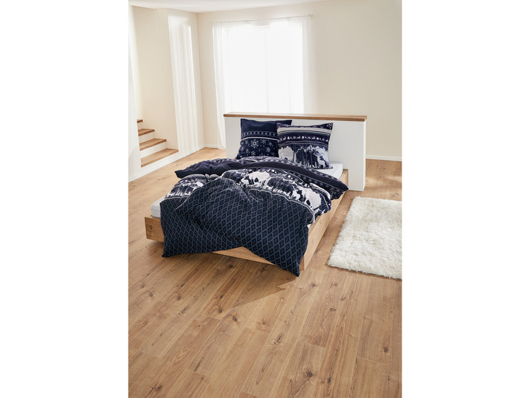 Ein Bett mit einer blauen Bettdecke mit winterlichem Design, mit zwei Kissen mit Schneeflocken.