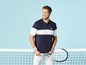 Mann mit einem Tennisschläger, trägt ein blaues Poloshirt mit weißem Streifen und weiße Hose.