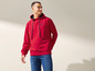 Ein Mann trägt eine rote Kapuzenjacke mit einem Logo und blaue Jeans.