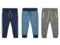 Drei Jungen-Jogginghosen, eine blaue mit weißen Streifen, eine blaue mit 'Wild One' und eine graue mit gelben Reißverschlüssen.
