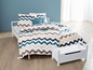 Ein weißes Bett mit einer Zickzack-Bettdecke und einer weißen Aufbewahrungsbox.