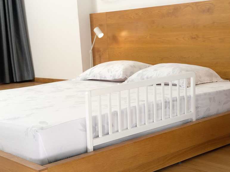 Ein Holzbett mit einem weißen Bettgitter.