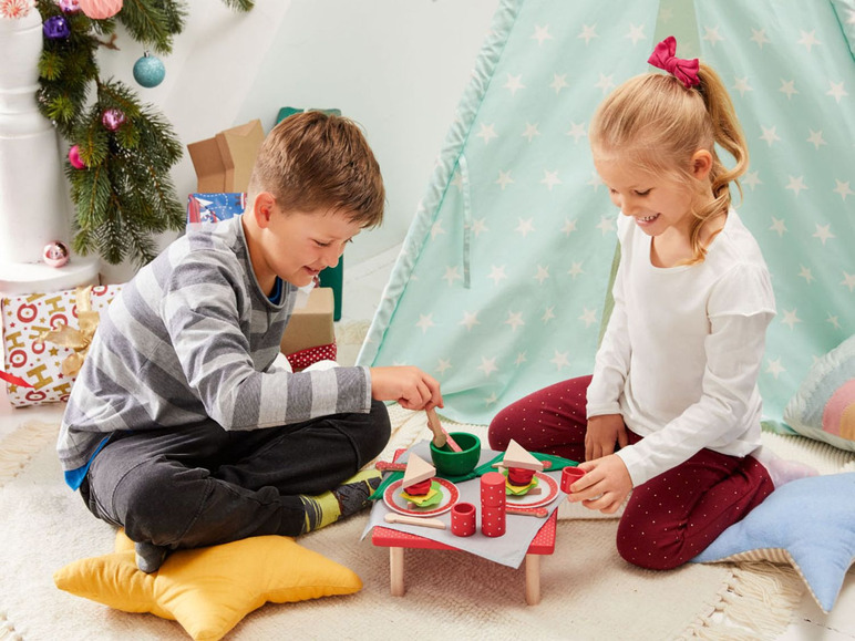 Zwei Kinder spielen mit einem hölzernen Spielzeug-Essens- und Trinkset in einem Zelt.