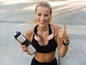 Eine Frau in Sportkleidung mit einer Wasserflasche und einem Nackenventilator zeigt Daumen hoch.