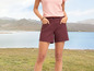 Frau in einem rosafarbenen T-Shirt und dunkelroten Shorts, die vor einem See steht.