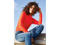Eine Frau trägt einen orangen Pullover und blaue Jeans.