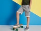 Junge mit grauen Shorts und grauen Schuhen auf einem Skateboard.