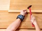 Eine Hand mit einem magnetischen Armband hämmert einen Nagel in ein Holzbrett.