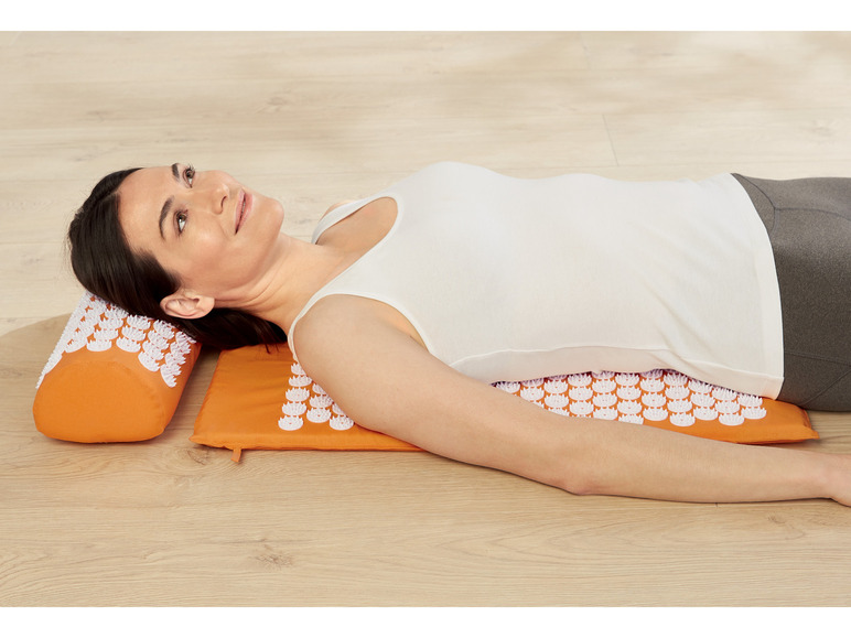 Eine Frau liegt auf einer orangen Akupressurmatte und einem Kissen.
