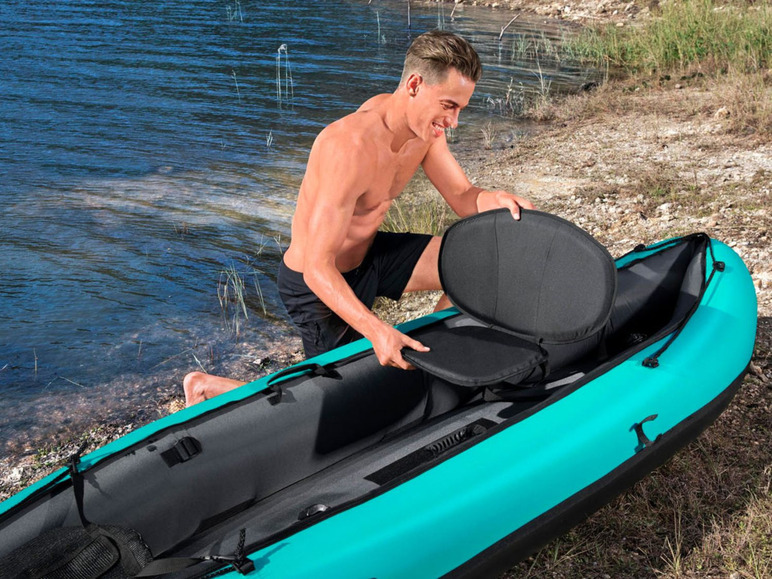 Ein Mann legt einen Sitz in ein aufblasbares Kajak am Wasser.