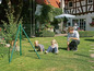 Kinder spielen in einem Garten mit Zaun und Schaukel.
