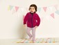Ein kleines Mädchen trägt eine rosa Fleecejacke und gestreifte Leggings.