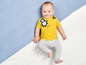 Baby in einem gelben T-Shirt mit Affen und grauen Leggings.