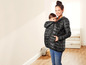 Eine Frau trägt eine schwarze Jacke mit einem Baby in einer Tragehilfe