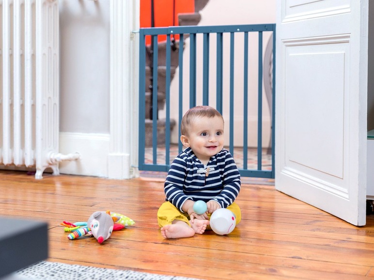 Ein Baby spielt mit einem Rassel und einem Stofftier auf dem Holzboden.