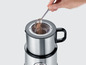 Eine Hand füllt Kakao in einen Krups Milchaufschäumer aus Edelstahl.