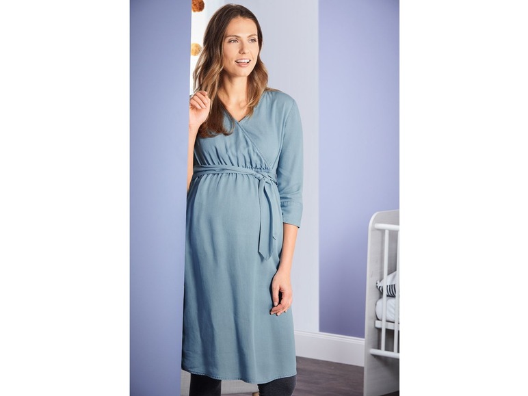 Eine schwangere Frau in einem blauen Wickelkleid.