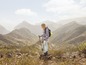 Eine Frau wandert mit Stöcken und Rucksack in einer Berglandschaft.