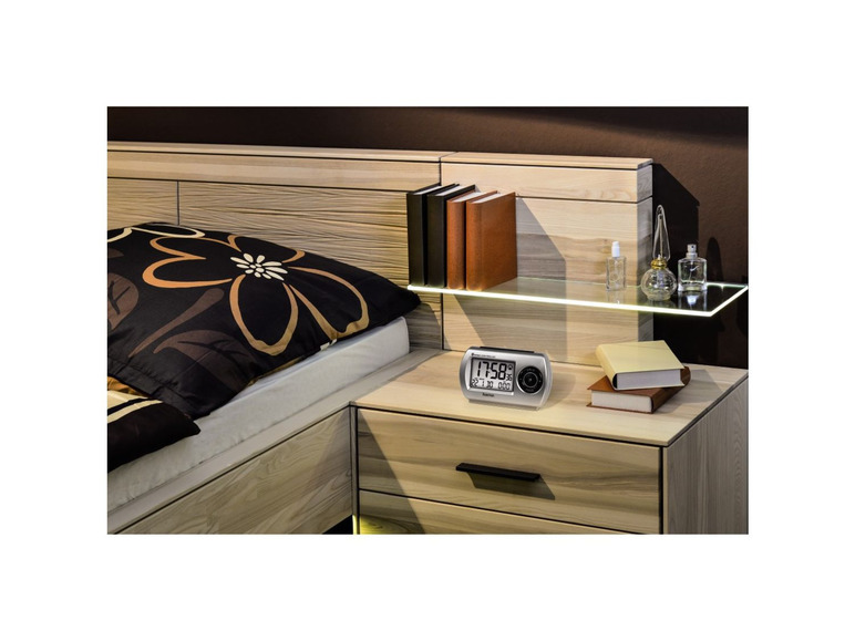 Ein Bett mit einem Nachttisch und einem Wecker mit digitaler Uhrzeit