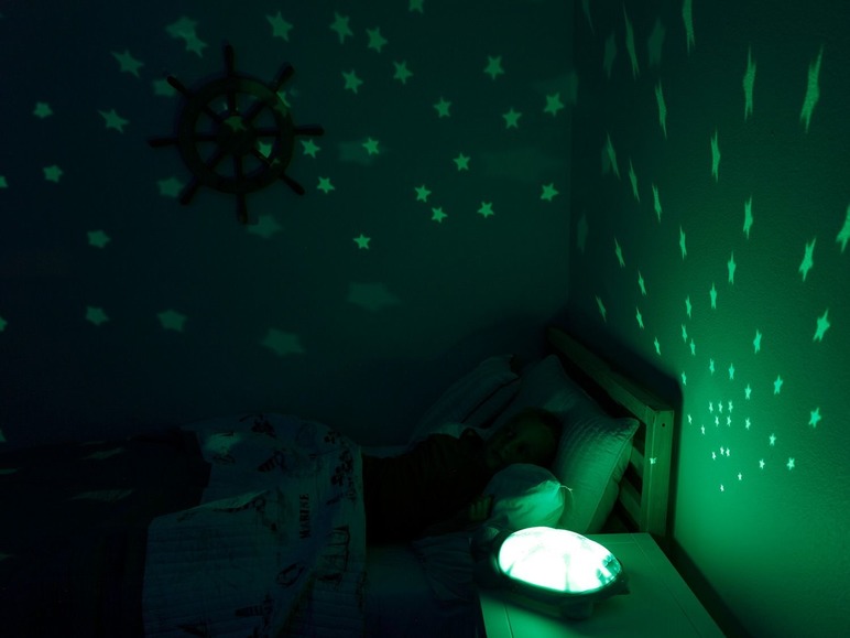 Ein Schlafzimmer mit einem Sternenprojektor und einem Kind im Bett.
