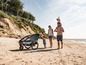 Eine Familie spaziert mit einem Qeridoo Kinderwagen am Strand.