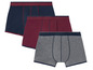 Drei Packungen Unterwäsche in dunkelblau, rot und grau.