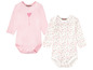 Zwei Baby-Bodys mit langen Ärmeln, einer rosa mit einem Herz und einer weiß mit Herzchenmuster.