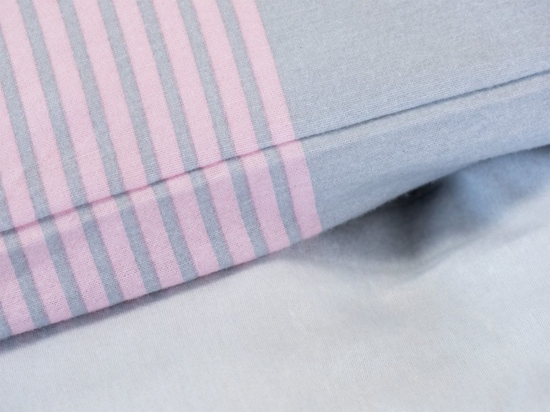 Eine rosa-graue gestreifte Bettdecke.