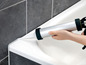 Eine Hand verwendet eine Silikonpistole, um eine Badewanne abzudichten.