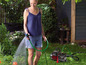Eine Frau benutzt eine Gardena Pumpe und einen Gartenschlauch, um ihren Garten zu bewässern.