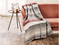 Eine gestreifte Decke in Rot- und Grautönen auf einem rosafarbenen Sofa.