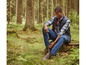 Mann im Wald mit Weste, Jeans und Timberland Stiefeln.