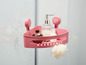 Ein rosa Eckregal für die Dusche mit Saugnäpfen, mit Shampoo, Seife und einem Schwamm.