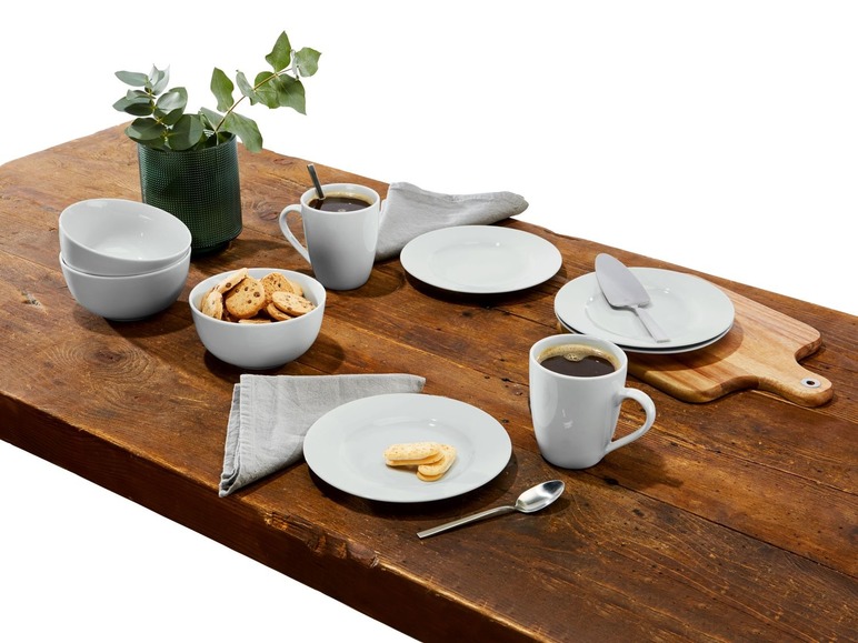 Weiße Tassen, Teller, eine Schüssel mit Keksen und ein Holzbrett auf einem Holztisch.