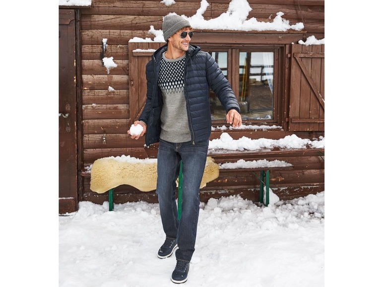 Mann in einer blauen Winterjacke, einem grauen Pullover und blauen Jeans im Schnee.
