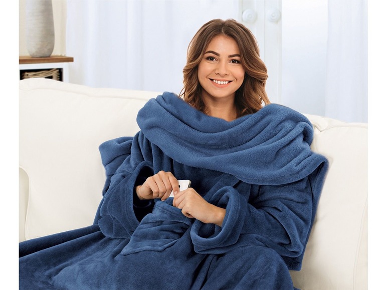 Eine Frau trägt eine blaue Fleece-Decke mit Ärmeln auf einer Couch.